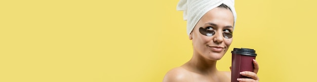 Young beautiful girl in a white towel on his head wears collagen gel patches under her eyes Mask under eyes treatment face The girl holds a glass of coffee in her hands