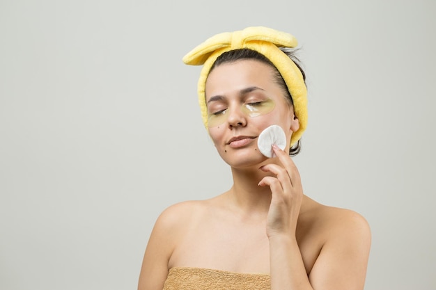 Young beautiful girl in a white towel on his head wears collagen gel patches under her eyes