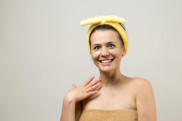 Young beautiful girl in a white towel on his head wears collagen gel patches under her eyes