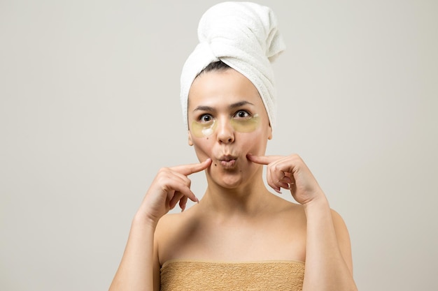 Young beautiful girl in a white towel on his head wears collagen gel patches under her eyes