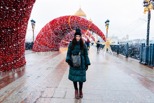 A young beautiful girl in winter stands on a bridge decorated for christmas