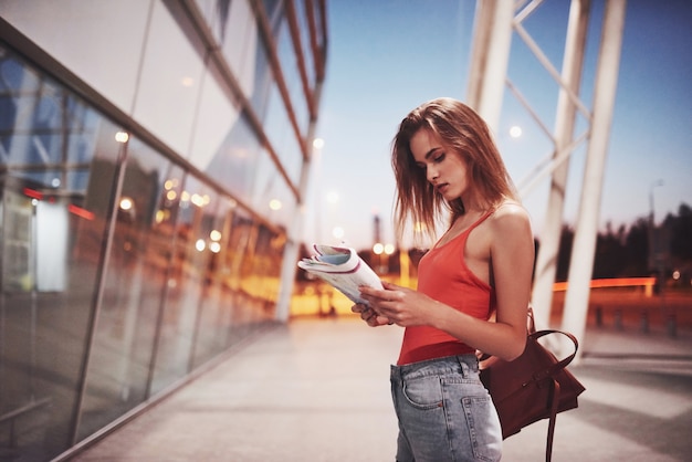 A young beautiful girl with a backpack behind her shoulders standing on the street near an airport.