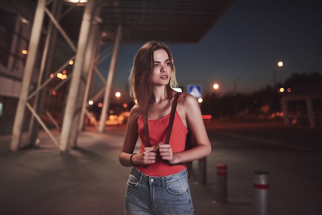 A young beautiful girl with a backpack behind her shoulders stands on the street near an airport