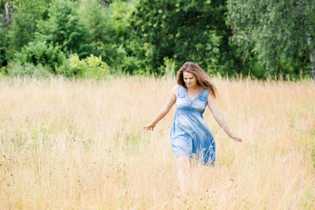 Young beautiful girl with beautiful long hair in a blue dress walks across the field