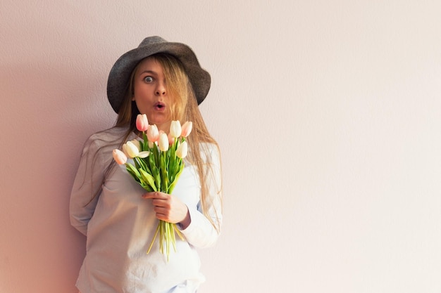 A young beautiful girl with blond dissolved long hair a felt hat on her head keeps spring flowers