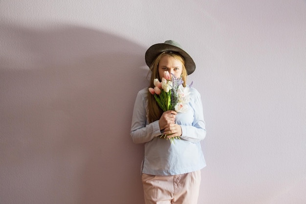 Photo a young beautiful girl with blond dissolved long hair a felt hat on her head keeps spring flowers