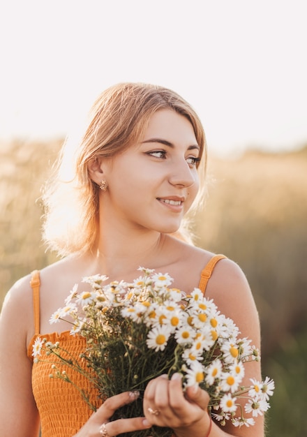 Young beautiful girl with a bouquet of daisies in a wheat field