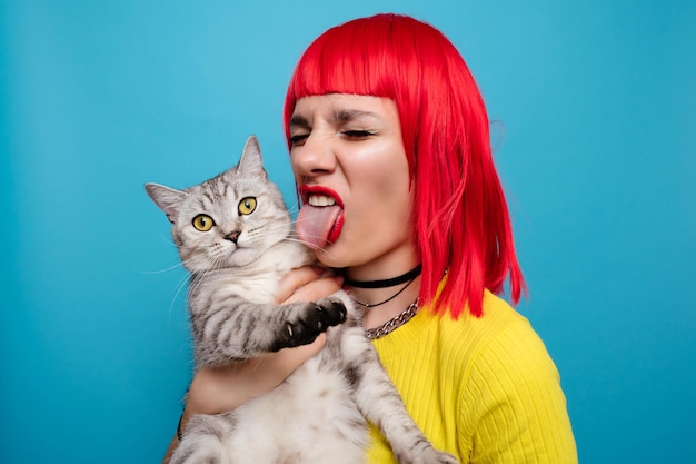 Photo a young beautiful girl with a cat in her arms isolated on a blue background expressive and funny expression on the face the friendship of the pet and the owner