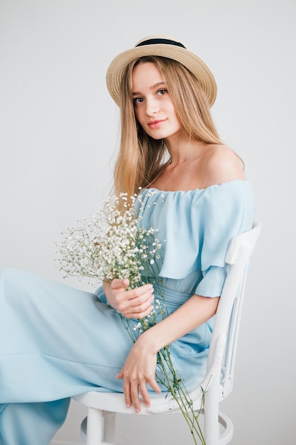写真 白い花の花束でポーズをとって長い髪と帽子を持つ若い美しい少女。調色。