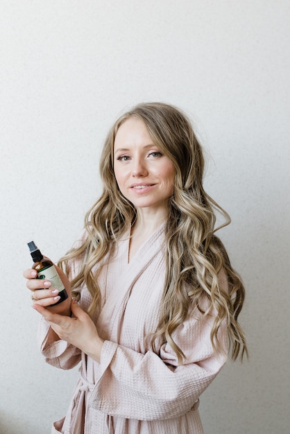 A young beautiful girl with long hair in a dressing gown holds a jar of natural cosmetics in her hands