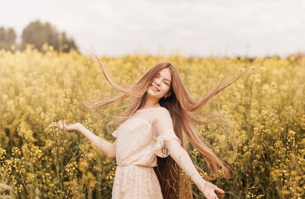 Young beautiful girl with long hair flying in the wind against the background of rapeseed field. breeze playing with girl's hair