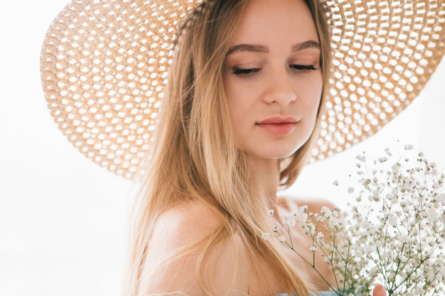 Giovane bella ragazza con capelli lunghi e cappello in posa con un mazzo di fiori bianchi. tonificante.