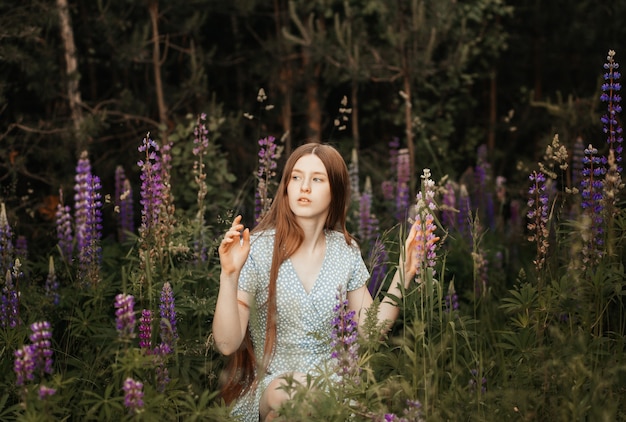 A young beautiful girl with long red hair in a clearing among the flowers. Lupines