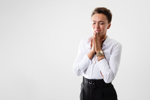 A young beautiful girl with short dark hair, makeup in a white shirt, black pants, with a wristwatch, bracelet and white manicure prays