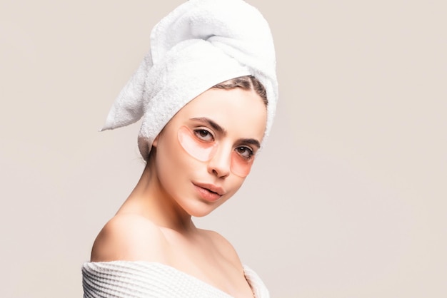 Young beautiful girl with a towel on head and a white robe girl cares for the skin using patches und