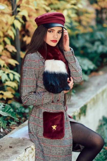 Young beautiful girl with very long hair wearing winter coat and cap in autumn leaves background