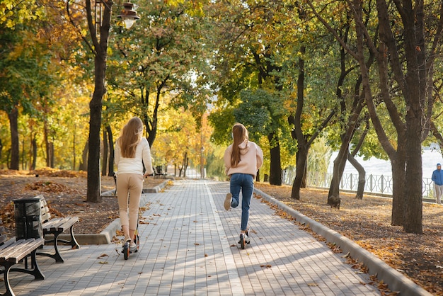 Молодые красивые девушки катаются в парке на электросамокате в теплый осенний день. Гулять в парке.