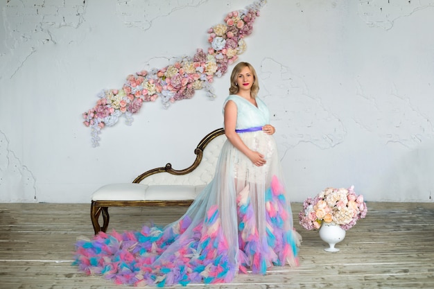 화려한 푹신한 드레스에 젊은 아름 다운 매력적인 임산부 꽃 다락방에 서있다. 행복한 임신