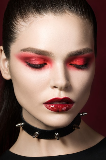 Young beautiful gothic woman with white skin red lips wearing black collar with spikes. Red smokey eyes.