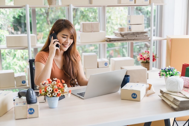 Young beautiful happy asian business woman in casual wear with smiley face is calling for receive orders of the customer with laptop at her startup home office, sme concept