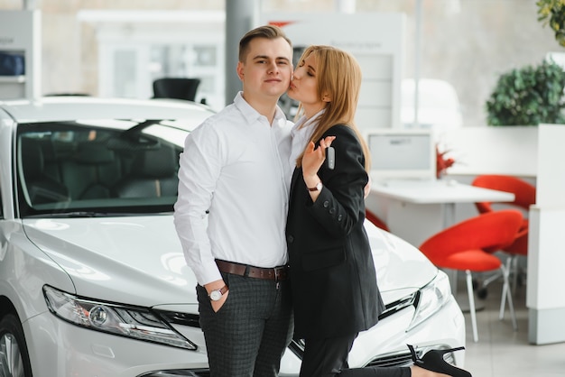 Young beautiful happy couple buying a car. Husband buying car for his wife in a salon. Car shopping concept.