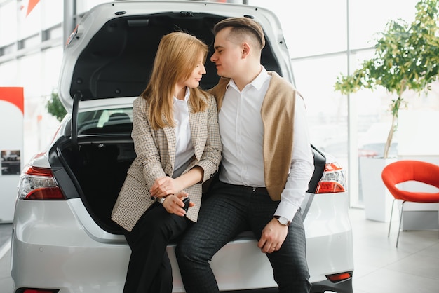 車を買う若い美しい幸せなカップル。夫がサロンで妻のために車を買う。カーショッピングのコンセプト。