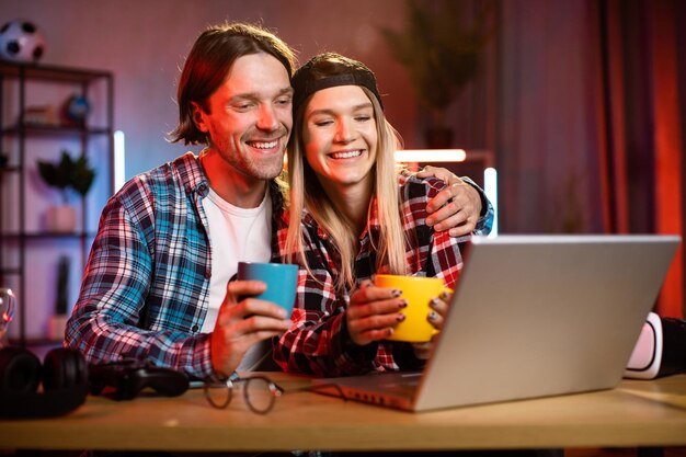 나무 테이블에 앉아 노트북을 사용하여 영화를 보는 젊은 아름다운 행복한 커플