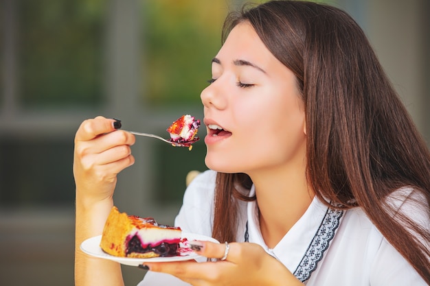 Young beautiful happy girl enjoying delicious fresh sweet cheesecake close up