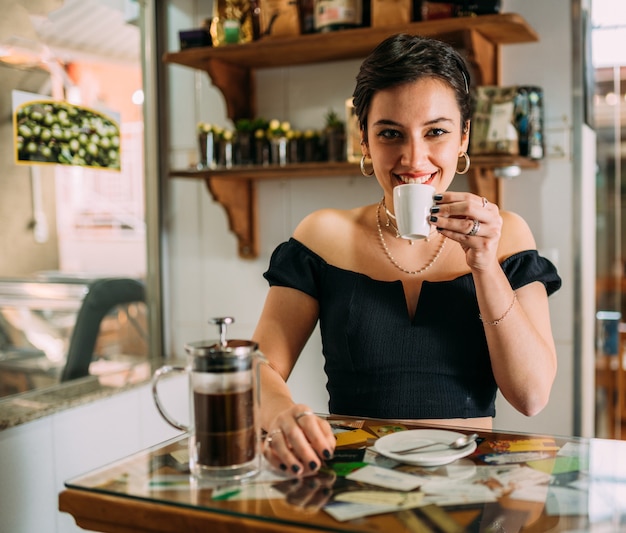Молодая красивая счастливая латинская женщина, наслаждающаяся кофе в уличном кафе