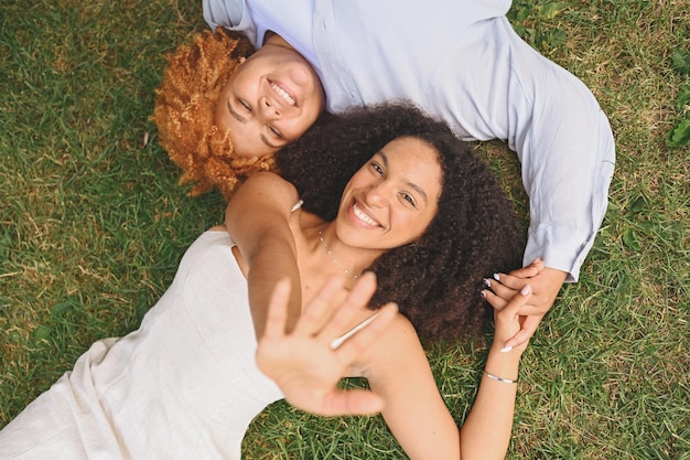 Young beautiful happy lesbian african american couple lying on grass laughing stretching out hands