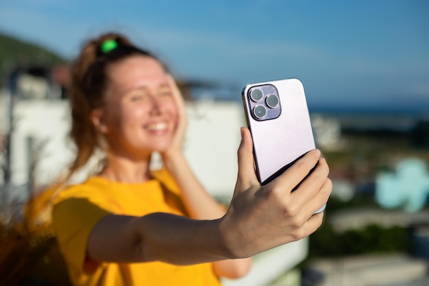 Young beautiful happy woman blogger is taking selfie picture of herself on frontal camera to social media of smartphone cell mobile phone smiling waving her hand having video call conversation