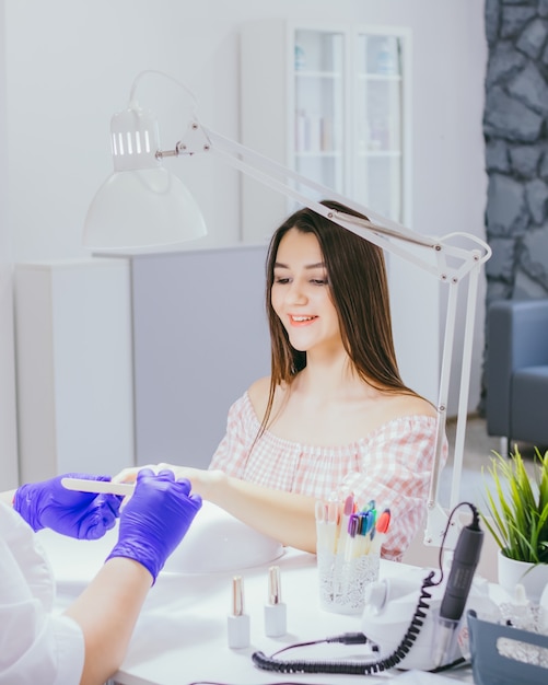 Young beautiful happy woman getting a manicure procedure in a beauty salon