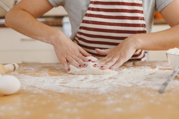 The young beautiful happy woman sitting at a table with flour, kneading dough and going to prepare a cakes in the kitchen. Cooking home. Prepare food close up.