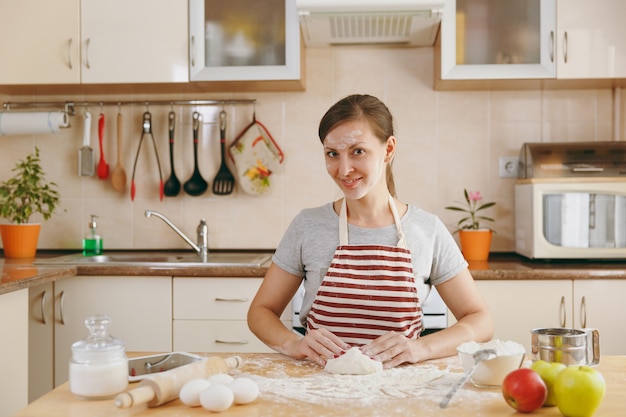 Молодая красивая счастливая женщина сидит за столом с мукой, замешивает тесто и собирается приготовить пирожные на кухне. Готовим дома. Готовить пищу.