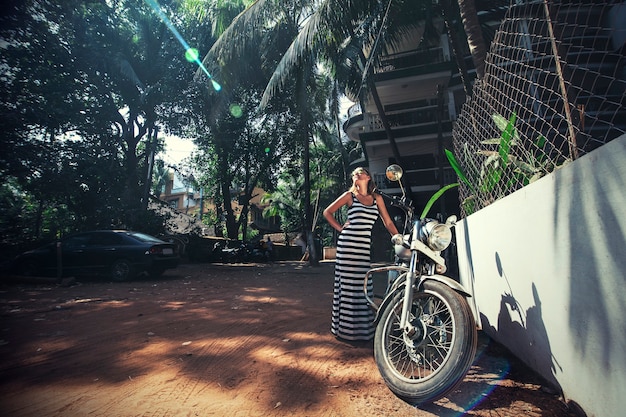 Young beautiful happy woman with bike on a tropical Asian street fashion dress