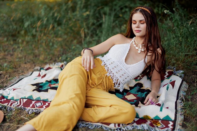 Young beautiful hippie woman lying on the ground in nature in the fall in eco clothes in yellow pants in the sunset light