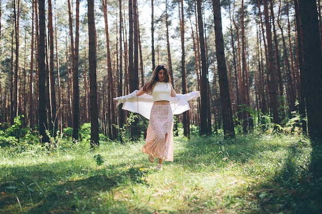 Young beautiful hippie woman walks in the summer forest laughs dances and enjoys life and nature