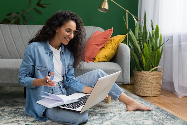 Young beautiful hispanic female student studying remotely online at home taking lecture notes