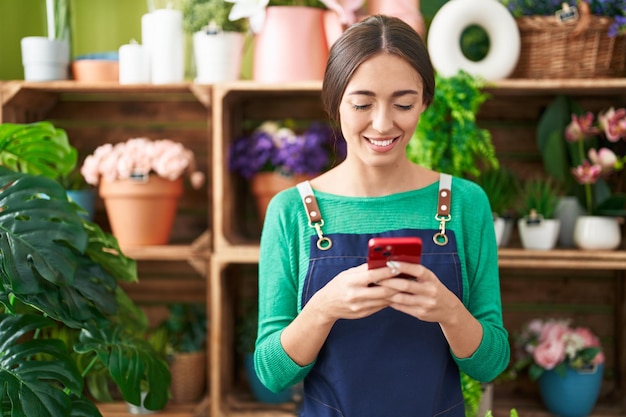 Young beautiful hispanic woman florist smiling confident using smartphone at flower shop