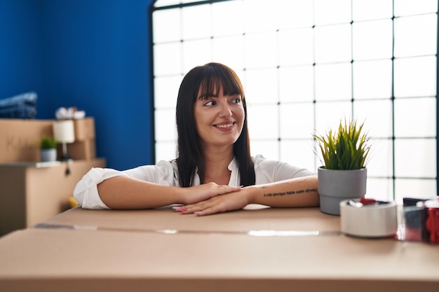 Young beautiful hispanic woman smiling confident leaning on package at new home