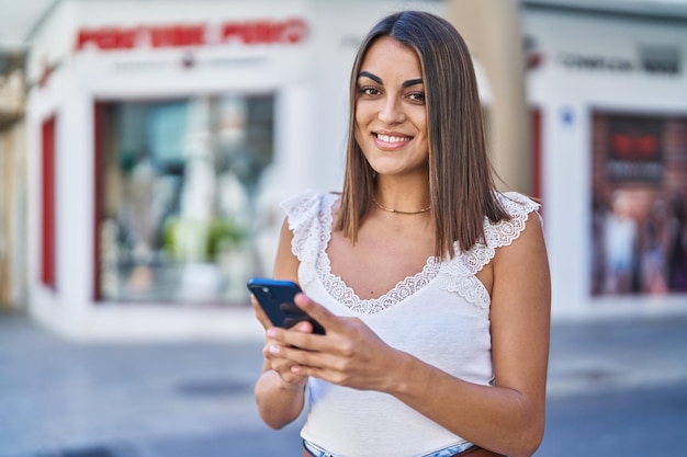 Young beautiful hispanic woman smiling confident using smartphone at street