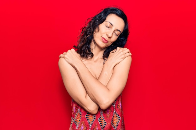 Young beautiful hispanic woman wearing casual clothes hugging oneself happy and positive smiling confident self love and self care