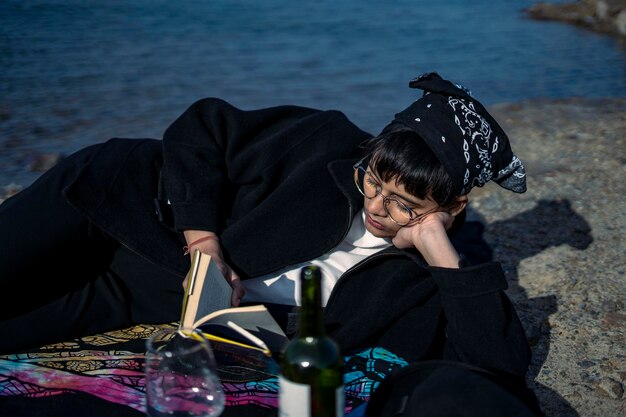 Foto giovane bella ragazza indiana che legge un libro mentre si appoggia a terra indossando un cappotto nero