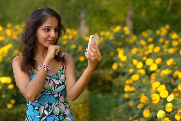 屋外の公園で電話を考えて使用する若い美しいインドの女性