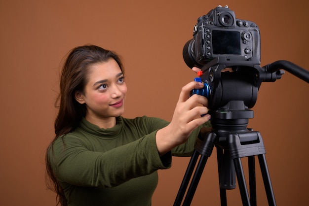 Young beautiful Indian woman vlogging against brown wall