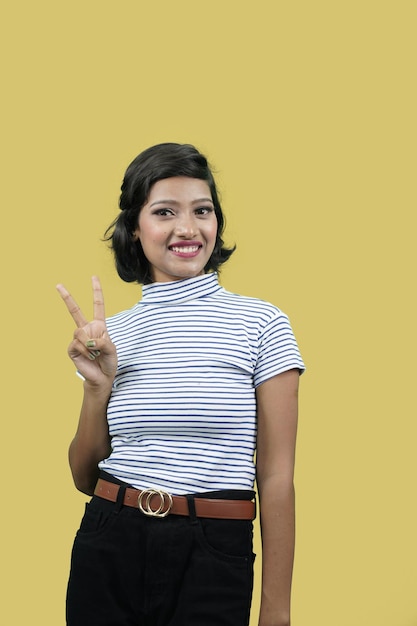 Foto giovane bella donna indiana su sfondo giallo sorridente guardando la fotocamera che mostra il segno della vittoria