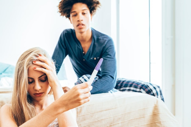 Young beautiful interracial couple in bed unhappy with pregnancy