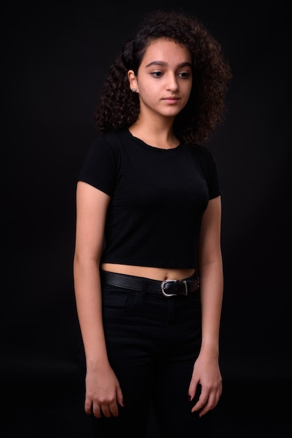 Photo young beautiful iranian teenage girl with curly hair against black wall