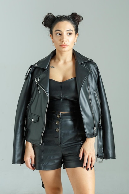 Young beautiful lady wearing leather clothes and stand on grey background High quality photo