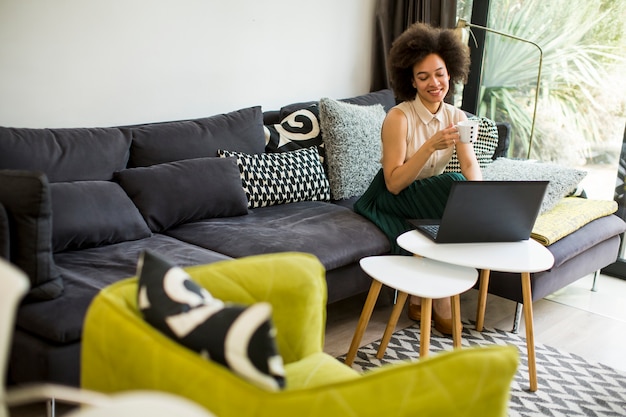 Young beautiful lady with curly hair work on the notebook while sit down on the couch at home